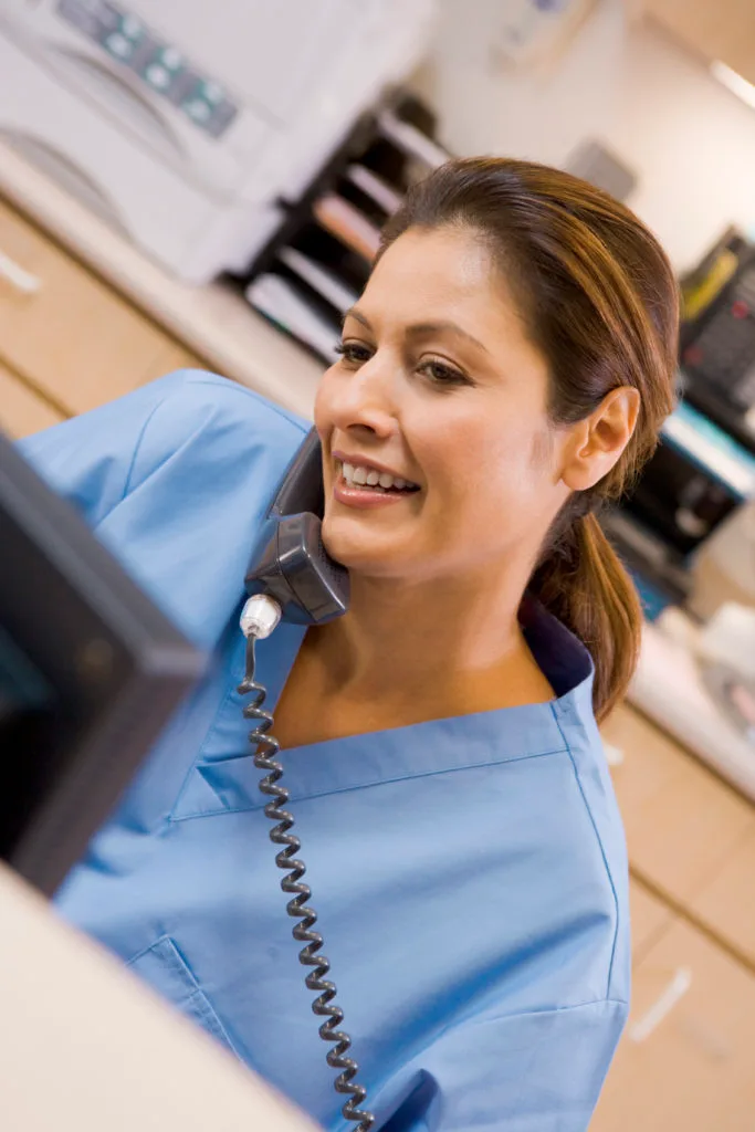 A Nurse On The Telephone At The Reception Area In A Hospital.