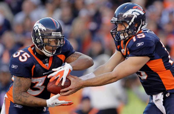 2 football players in navy blue and orange uniforms, one is passing a football to the other one