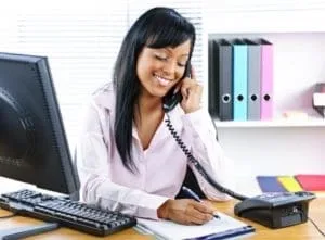 A receptionist sitting at a desk in a dental office, answering a phone call.