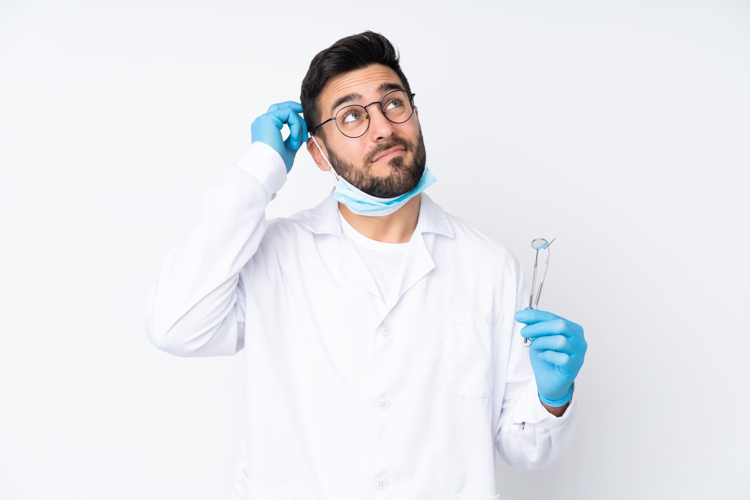Male dentist with beard, standing and looking uncertain, holding dental equipment