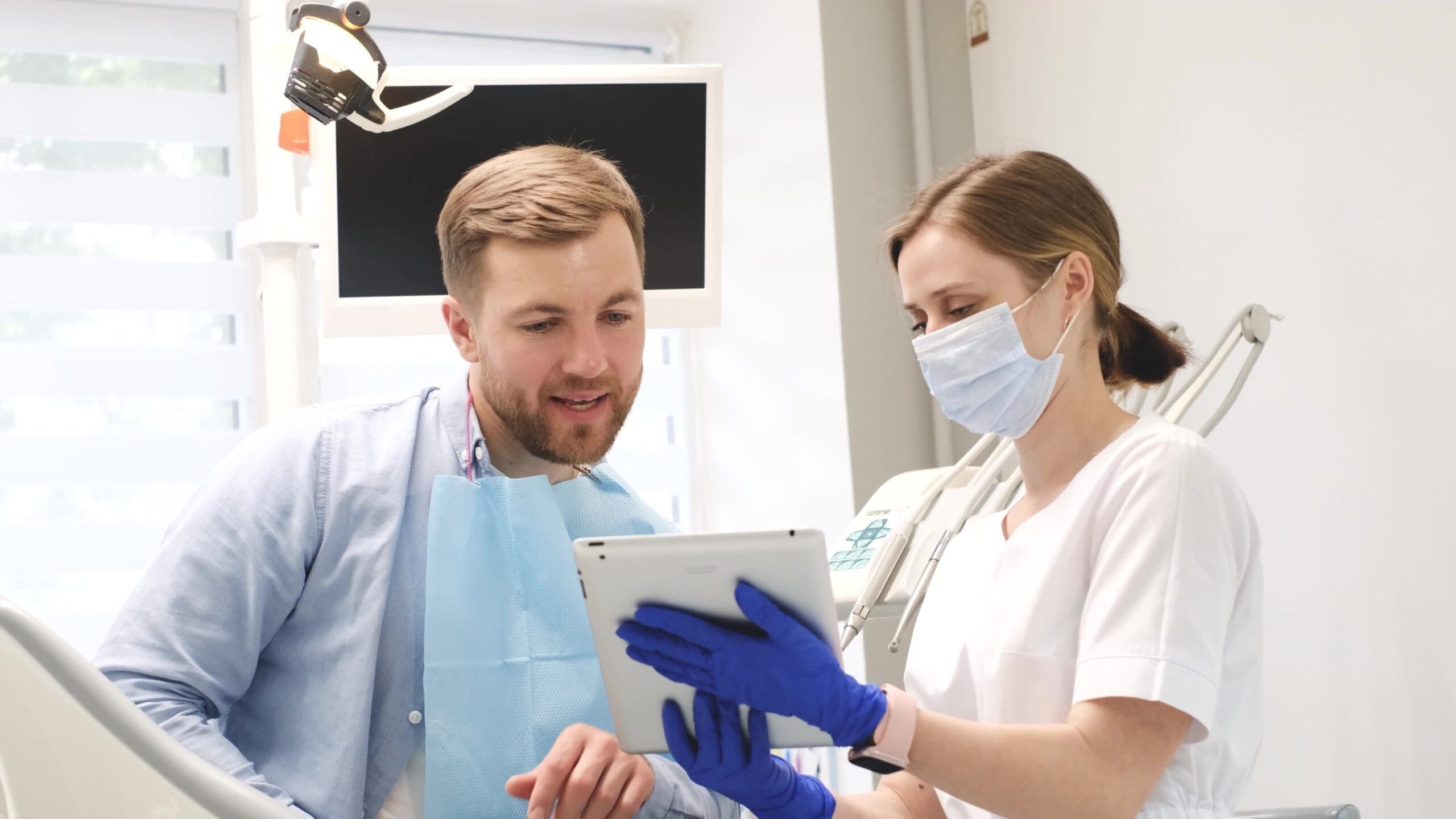 Male dental patient with female dentist, with an ipad in front of them, talking.