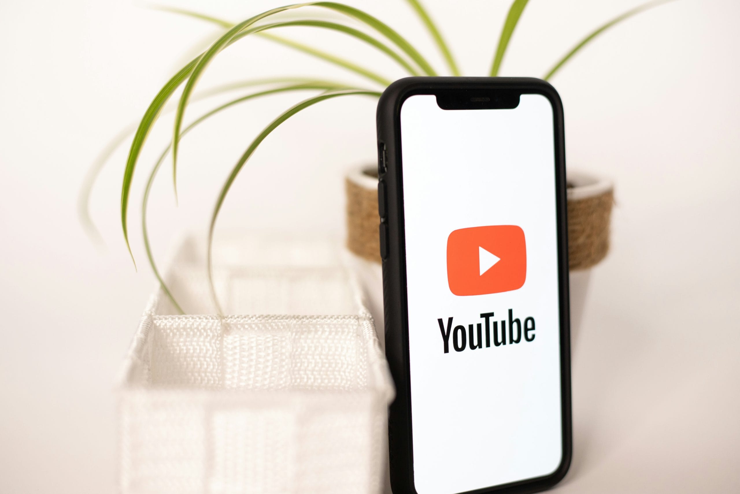 A phone with the youtube logo on it. Sitting on a table with a nice looking plant.