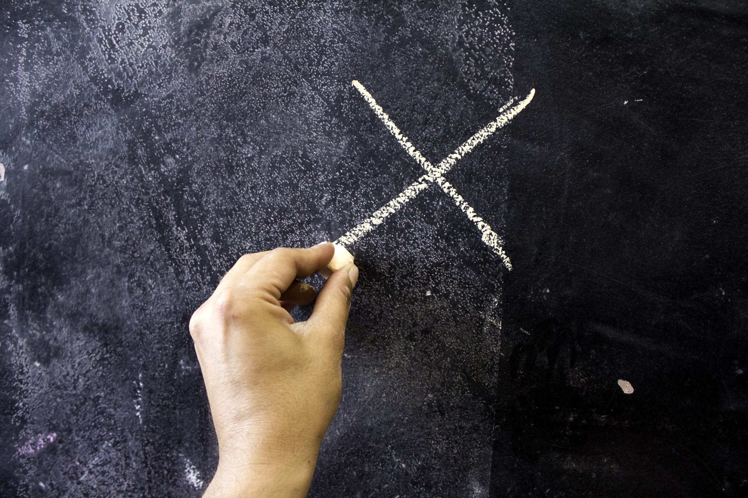 a person's hand writing an X on a chalk board