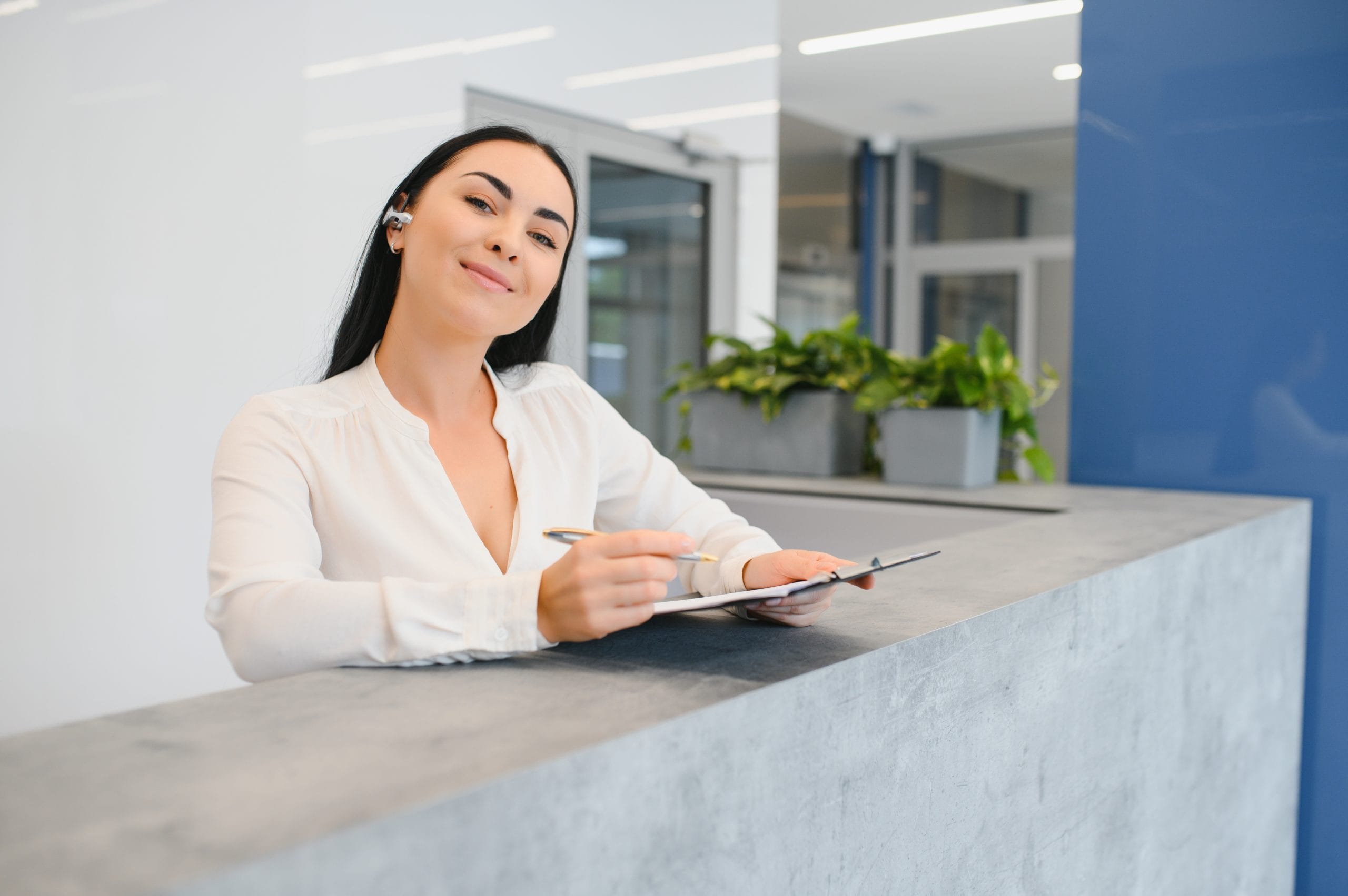 an attractive women behind a desk holding a scheduling clipboard
