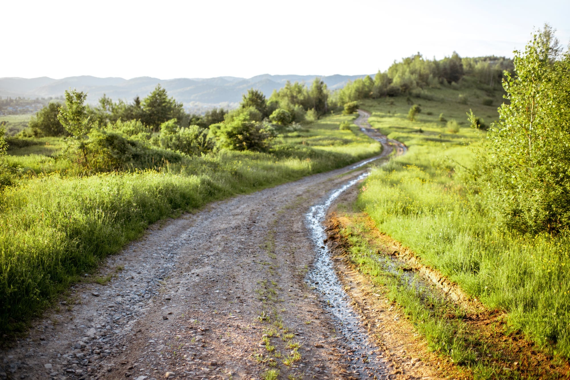 A narrow winding road leading through a scenic landscape toward a bright horizon.