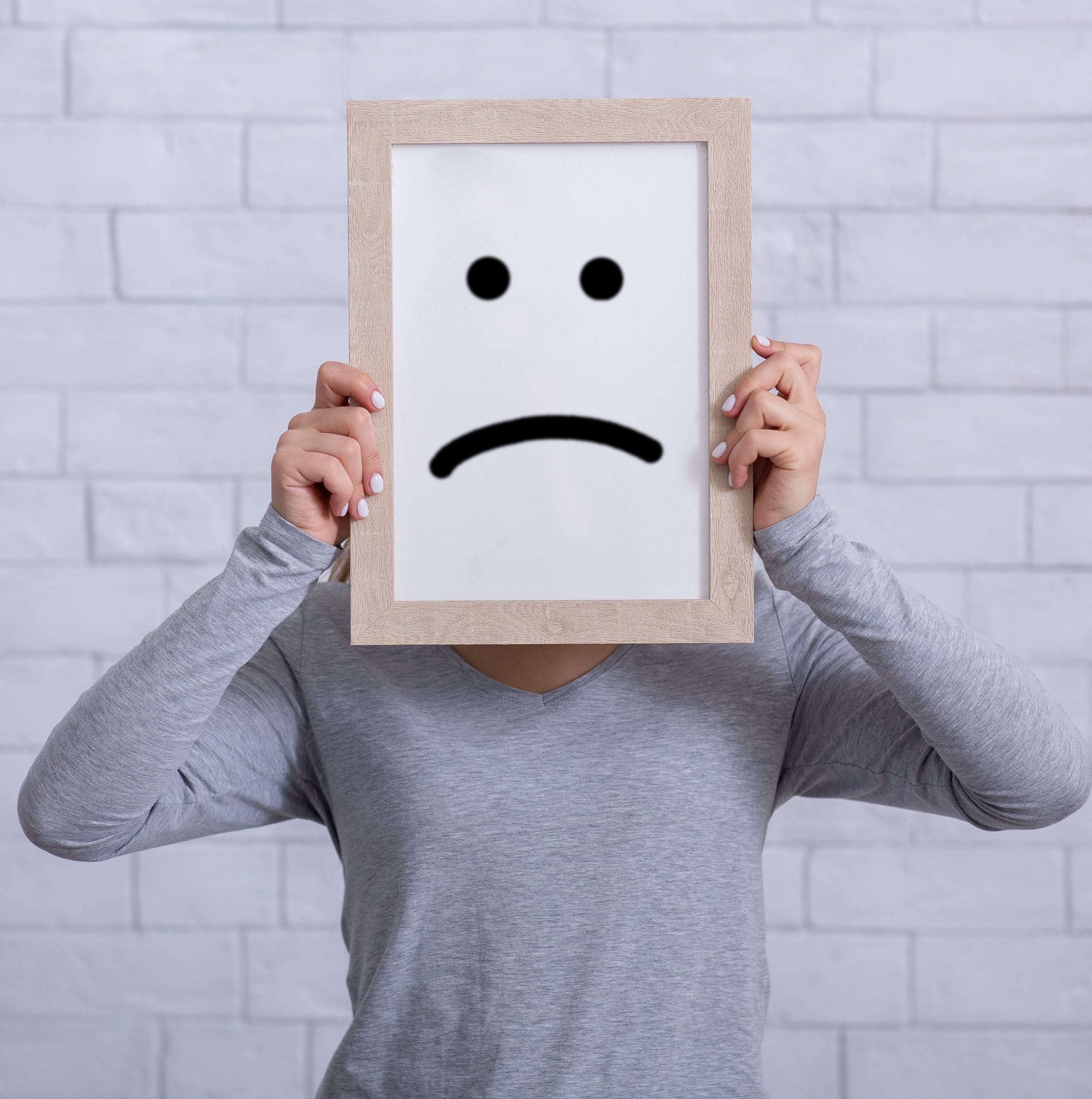 A person holding a sad face sign over their face.